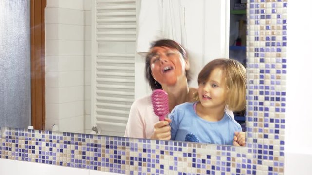 Happy mother and daughter dancing in bathroom in front of mirror