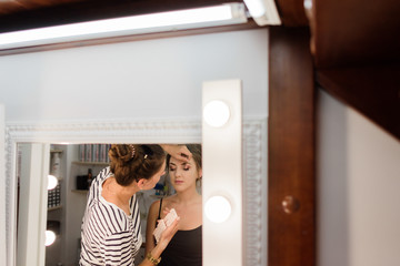 Artist does make-upf for a woman sitting before the mirror