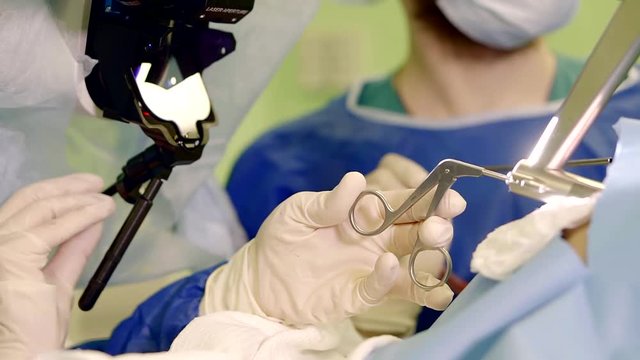 surgeon is cauterizing by laser a soft tissues of neoplasm in body of patient, assistant is pumping blood