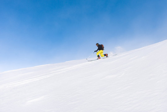 Man skiing telemark style on steep slope on a bright day