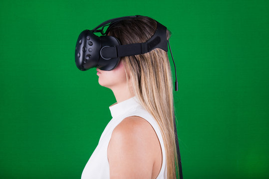 attractive woman wearing virtual reality headset and immersed into her experience in green screen studio