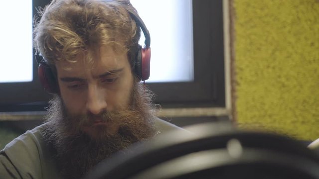 Beardy drummer listens to the sound of his electric drums with red headphones.