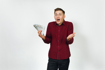 Handsome cheerful positive satisfied caucasian lucky young happy business man 25-30 years in red shirt holding wad of cash money on white background isolated for advertisement. Winner with dollars.