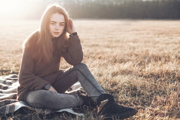 A young woman in sweater sitting on a field.