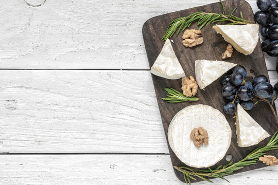 camembert cheese with grapes, walnuts and rosemary on wooden cutting board