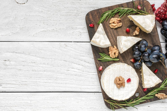 camembert cheese with grapes, pomegranate seeds, walnuts and rosemary on wooden cutting board