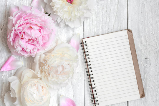 pink and white peony flowers with blank lined notebook on white wooden table