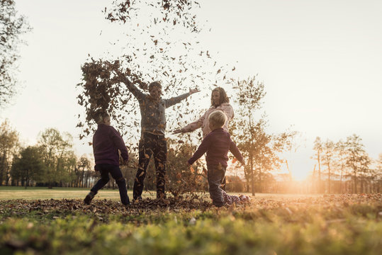 Young family rejoicing in an autumn sunset standing throwing leaves in the air