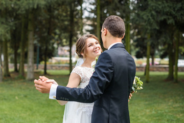 Just married couple dancing valse outdoor, free space. Bride and groom hugs, blurred green grass background. First wedding dance concept