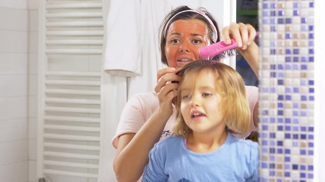 Woman brushing hair of little daughter while singing happy