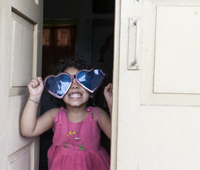 A kid wearing blue heart shaped sunglass and lsughing