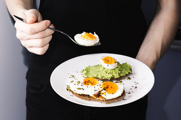 sandwich with fresh vegetables, avocado, hard-boiled eggs and pumpkin seeds with olive oil and bread. healthy diet or vegetarian food on a white background. salad with yolks on toast in hands
