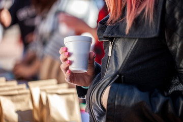 Woman with painted pink nails and leather jacket holding coffee cup, focus on hand and cup