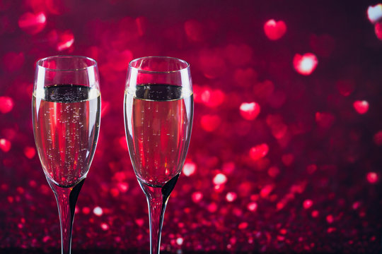Two glasses of champagne with red heart shape bokeh on background.