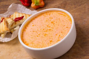 Traditional Ukrainian Russian vegetable borsch on the white bowl. Old wooden background. Sour cream sauce, red hot peppers, mini bread toast with garlic.