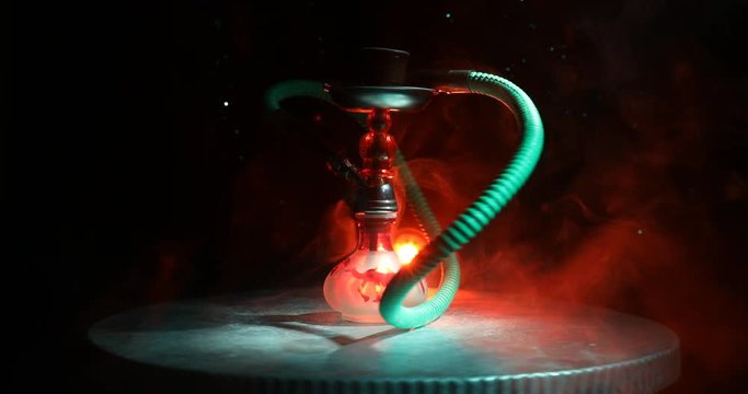 Hookah hot coals on shisha bowl on orange (like fire) clouds of steam on dark background. Stylish oriental shisha. Shisha Concept. On rotating display. 