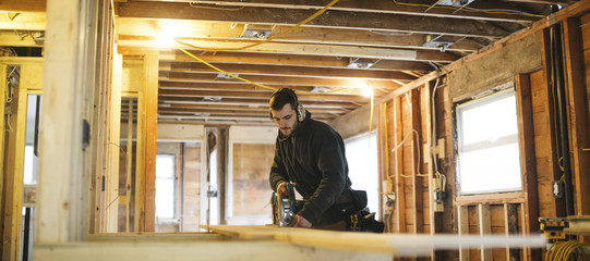 Panoramic of young carpenter using skill saw inside