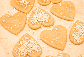 Closeup food background with cookie dough, cookies in form of hearts and sesam seeds 