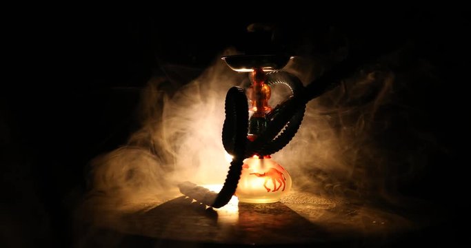 Hookah hot coals on shisha bowl on orange (like fire) clouds of steam on dark background. Stylish oriental shisha. Shisha Concept. On rotating display. 
