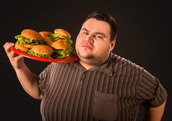 Diet failure of fat man eating fast food. Happy smile overweight person who crazy makes squint for fun eating huge hamburger on fork. Bachelor food. Man suffers from gluttony.