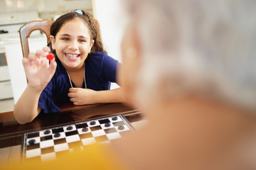 Grandma Playing Checkers Board Game With Granddaughter At Home