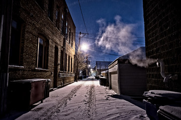Dark, cold Chicago winter alley with snow, ice and a steaming vent at night.