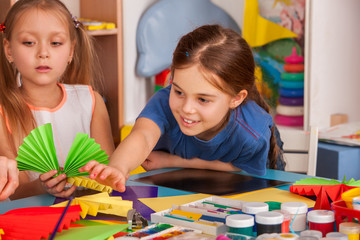 School children with scissors in kids hands cutting paper with teacher in class room. Development and social lerning. Children's project in kindergarten. Newcomer in a children's team.