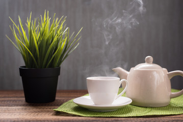 hot tea with steam and teapot on a table background. hot tea and teapot on leaf shape mat