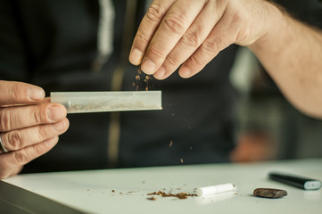Man preparing hashish joint rolling marijuana cigarette for smoking