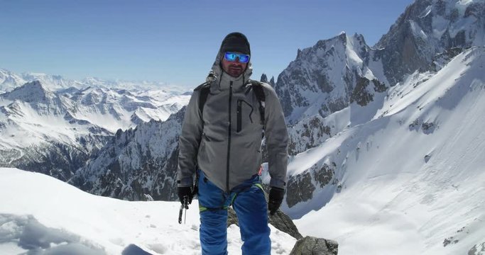 Climber mountaineer man portrait on snowy mount top in sunny day.Mountaineering ski activity. Skier people winter snow sport in alpine mountain outdoor.Front view.Slow motion 60p 4k video