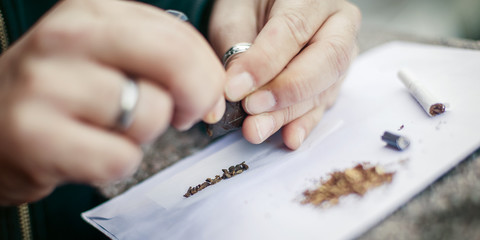 Man preparing hashish joint rolling marijuana cigarette for smoking
