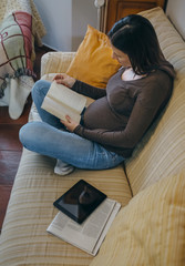 Pregnant woman reading a book sitting on the couch