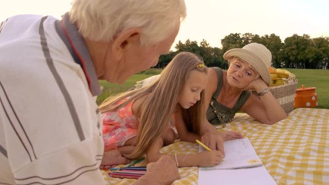 Girl drawing with pencil outdoors. Grandmother giving advice to her granddaughter how to draw, nature background. Importance of help and support for kids.