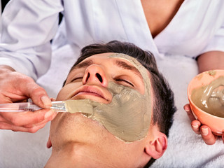 Obraz na płótnie Canvas Mud facial mask of woman in spa salon. Massage with clay full face. Girl on with therapy room. Female lying wooden spa bed. Removing black dots. Anti-aging cosmetic mask.