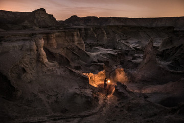 woman with lantern walking through a spooky rugged canyon at night