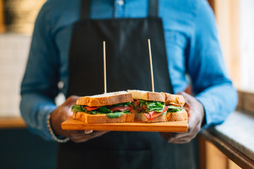 Bartender holding a pastrami sandwich in a small restaurant.