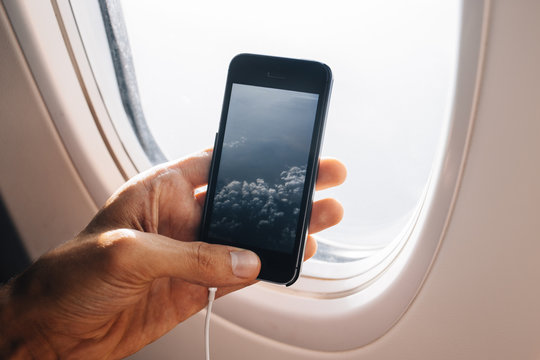 Detail of the man hand taking photo with smartphone through airplane window