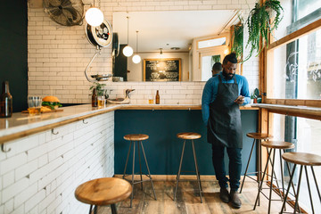 Portrait of a young black man using phone in a pastrami sandwich bar.