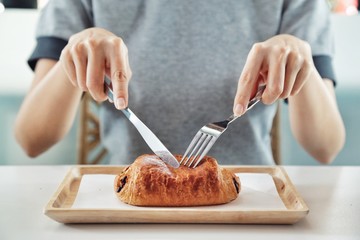 woman using fork and knife eating chocolate croissant on a small wooden tray covered with parchment paper / wax paper