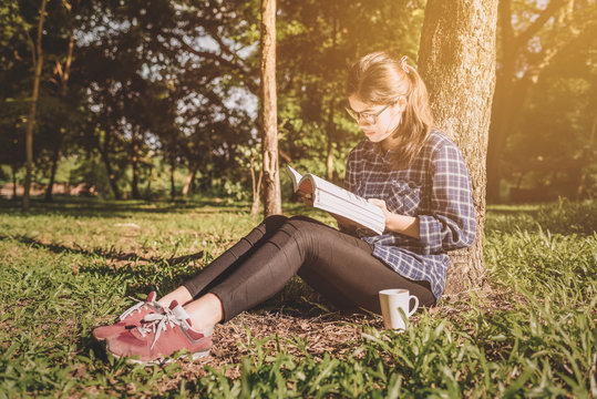 The girl sitting on a green grass with cup of coffee and reads the book