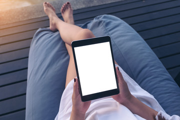 Top view mockup image of a woman using black tablet pc with blank white desktop screen while sitting with feeling relaxed