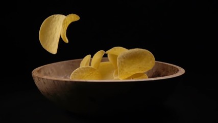 Potato chips are poured into a wooden bowl on a black background