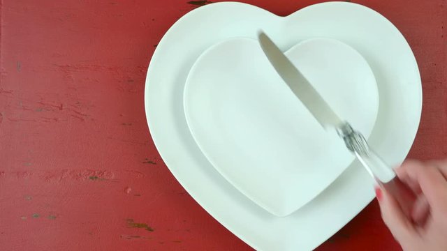 Valentine romantice place setting with heart shaped plates and red rose, time lapse overhead on red rustic wood table.