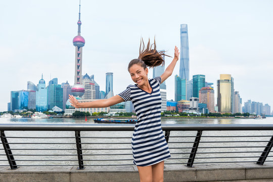 Happy Asian woman having fun dancing of joy in front of Shanghai skyline on The Bund. China travel healthy lifestyle. Happiness concept in urban city. Young adult in her 20s living active life.