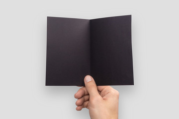 Mockup A6 empty blank black postcard horizontally bent in half holds the man in his hand. Isolated on a gray background