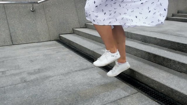 Closeup slow motion footage of stylish girl in sneakers jumping and running down stone stairs on street
