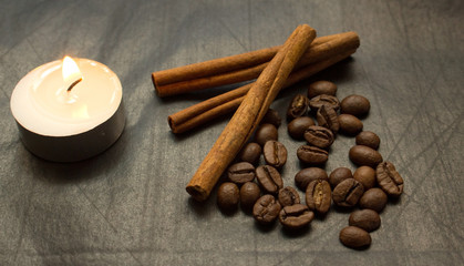 cinnamon sticks, coffee beans, lighted candle on a black background