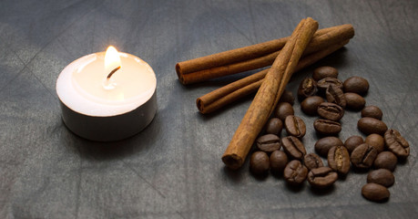 cinnamon sticks, coffee beans, lighted candle on a black background