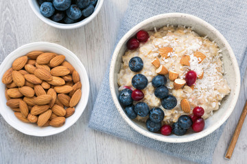 Oatmeal porridge bowl with blueberries, cranberries, almonds and coconut flakes on gray background. Top view, closeup