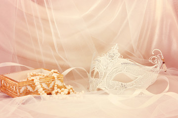 Image of delicate and elegant white venetian mask in front of tulle background.